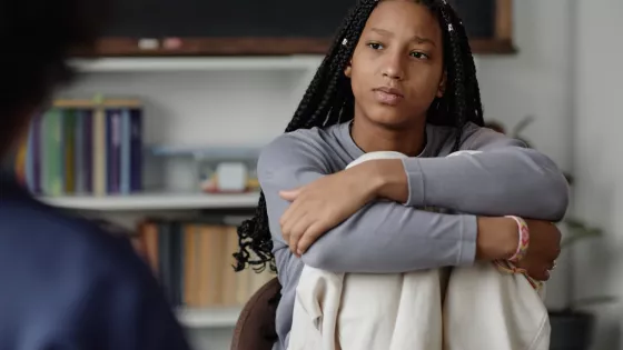 A teenage girl looks serious, with her arms wrapped around her knees.