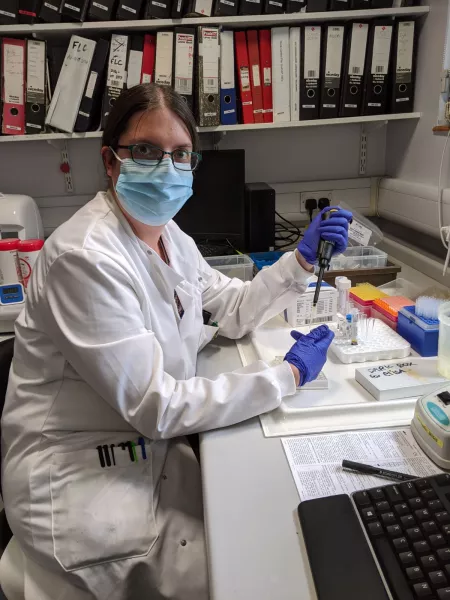 A masked biochemist in a lab coat works in a laboratory. 