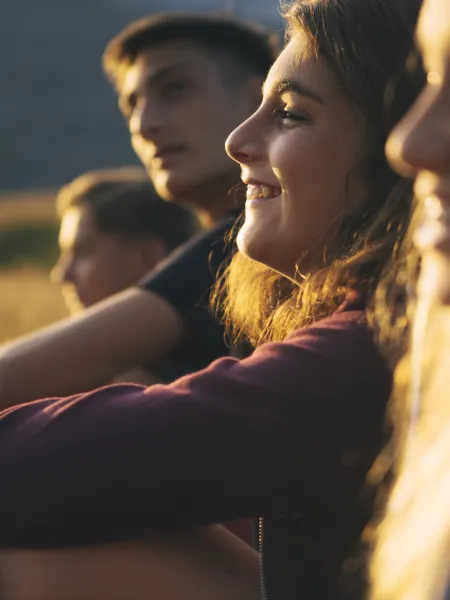 A group of teenagers sit smiling in a row outside in the low light of sunset.